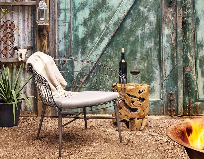 A raw teak stool by Four Hands being used as a drink table next to a wire chair